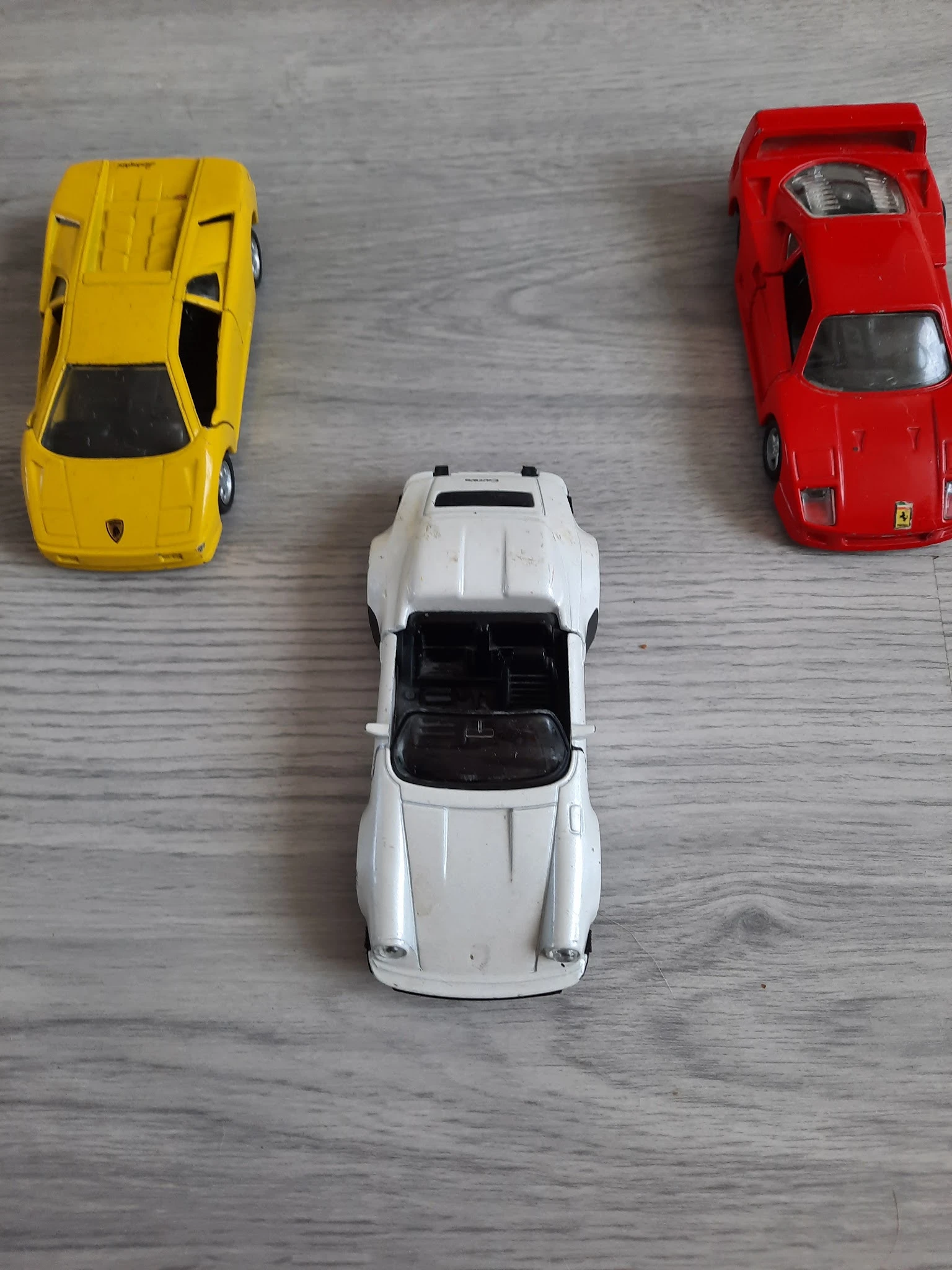 Drie miniatuurauto's op houten oppervlak: gele, witte en rode speelgoedauto's