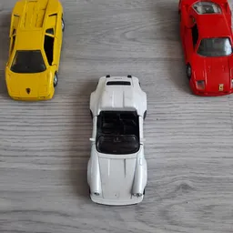 Drie miniatuurauto's op houten oppervlak: gele, witte en rode speelgoedauto's