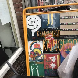 Verzameling van vintage posters en kunstwerken tegen een oranje kader, waaronder werk van Kraayenest