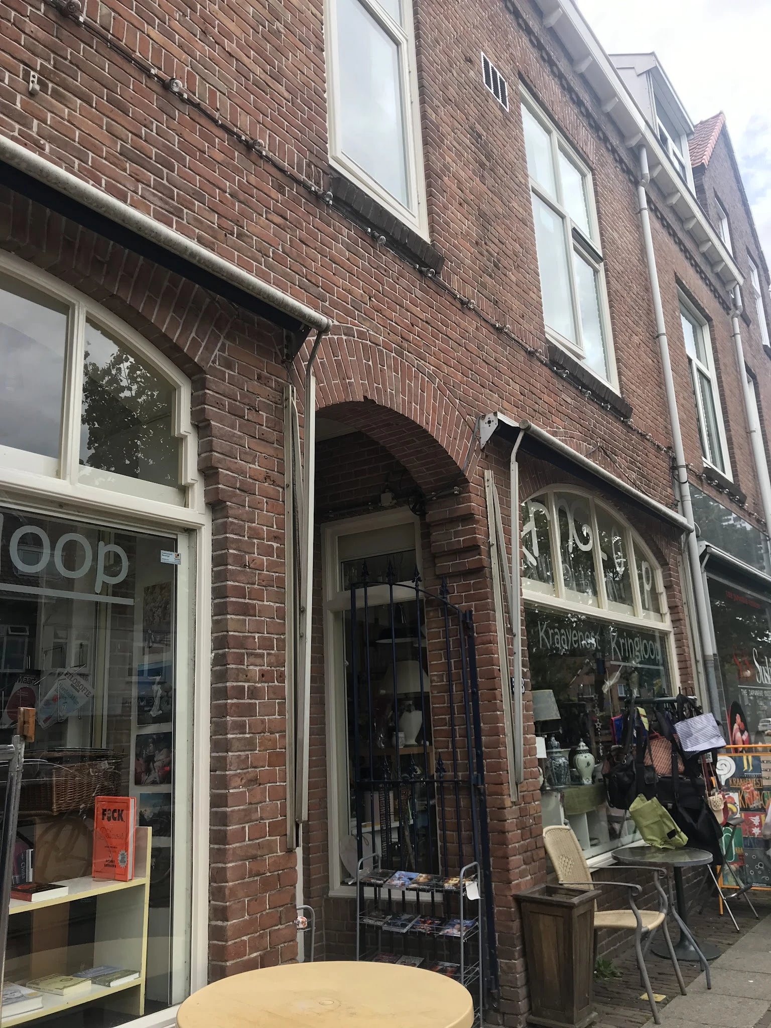 Gevel van kringloopwinkel met baksteen, witte raamkozijnen en ingang onder booggewelf