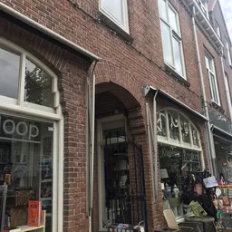 Gevel van kringloopwinkel met baksteen, witte raamkozijnen en ingang onder booggewelf