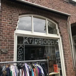 Gevel van kringloopwinkel met witte raamkozijnen en uithangbord, kledingrek met hangers zichtbaar in etalage