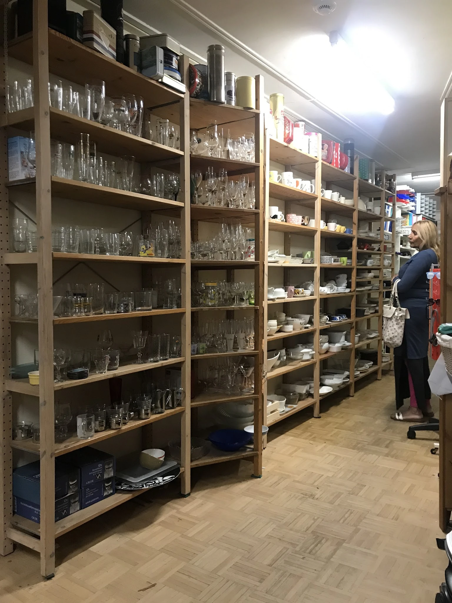 Stellingen met glazen serviesgoed en huishoudartikelen in een kringloopwinkel