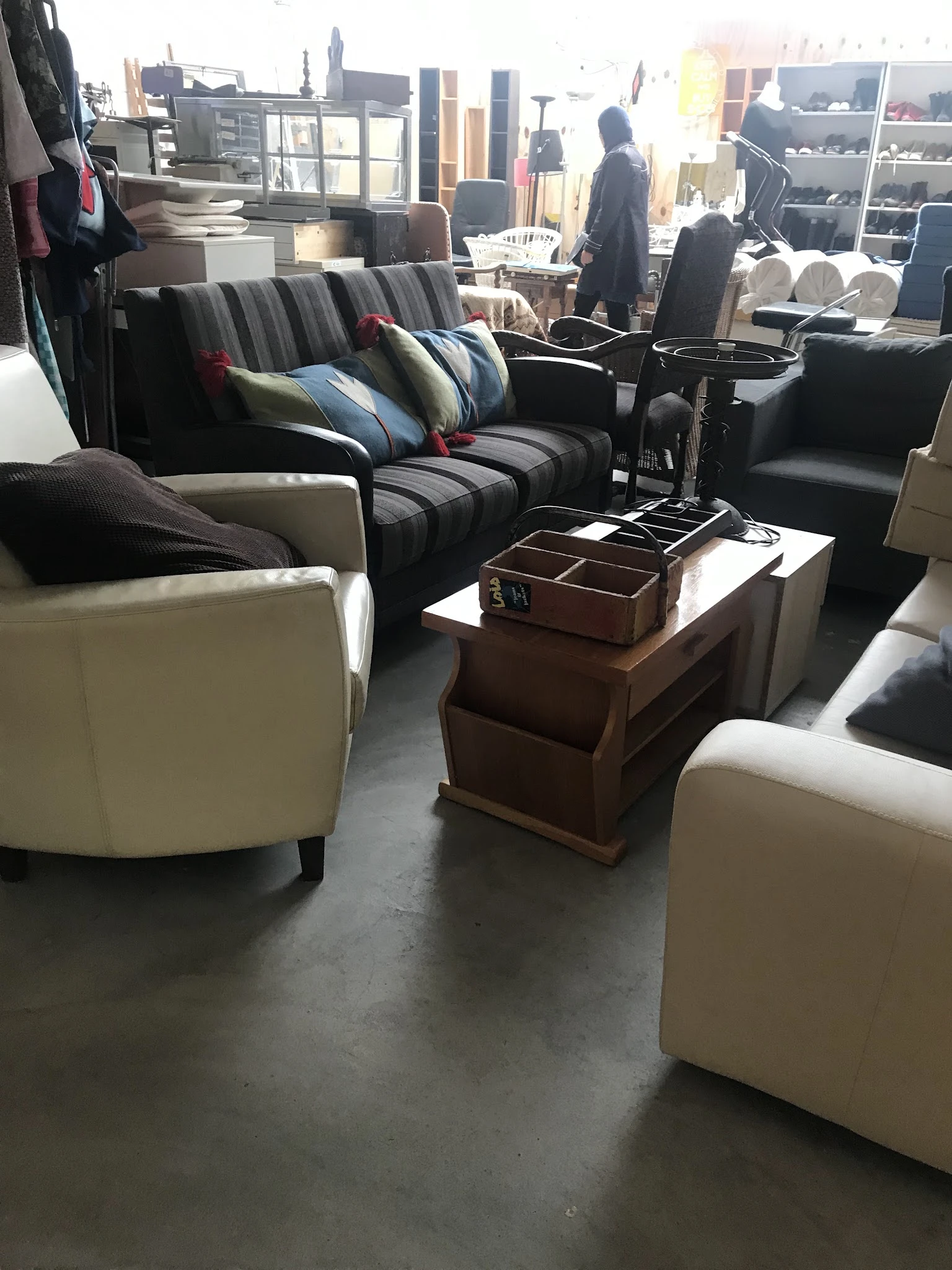 Uitgestalde meubels in kringloopwinkel: crèmekleurige fauteuils, gestreepte banken met kussens en houten salontafel met decor