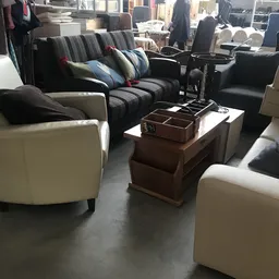 Uitgestalde meubels in kringloopwinkel: crèmekleurige fauteuils, gestreepte banken met kussens en houten salontafel met decor