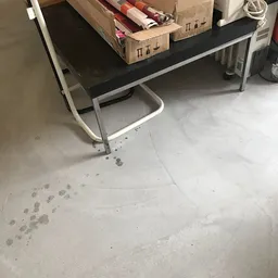 Betonnen winkelsvloer met voetafdrukken en een tafel met witte poten
