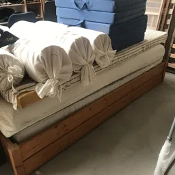 Tweepersoonsmatras met witte lakens en decoratieve kussens op houten bedframe