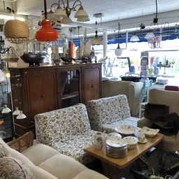 Winkelvloer met meubels: tweepersoonsbank, fauteuils, houten dressoir en hanglampen, achter grote ramen.