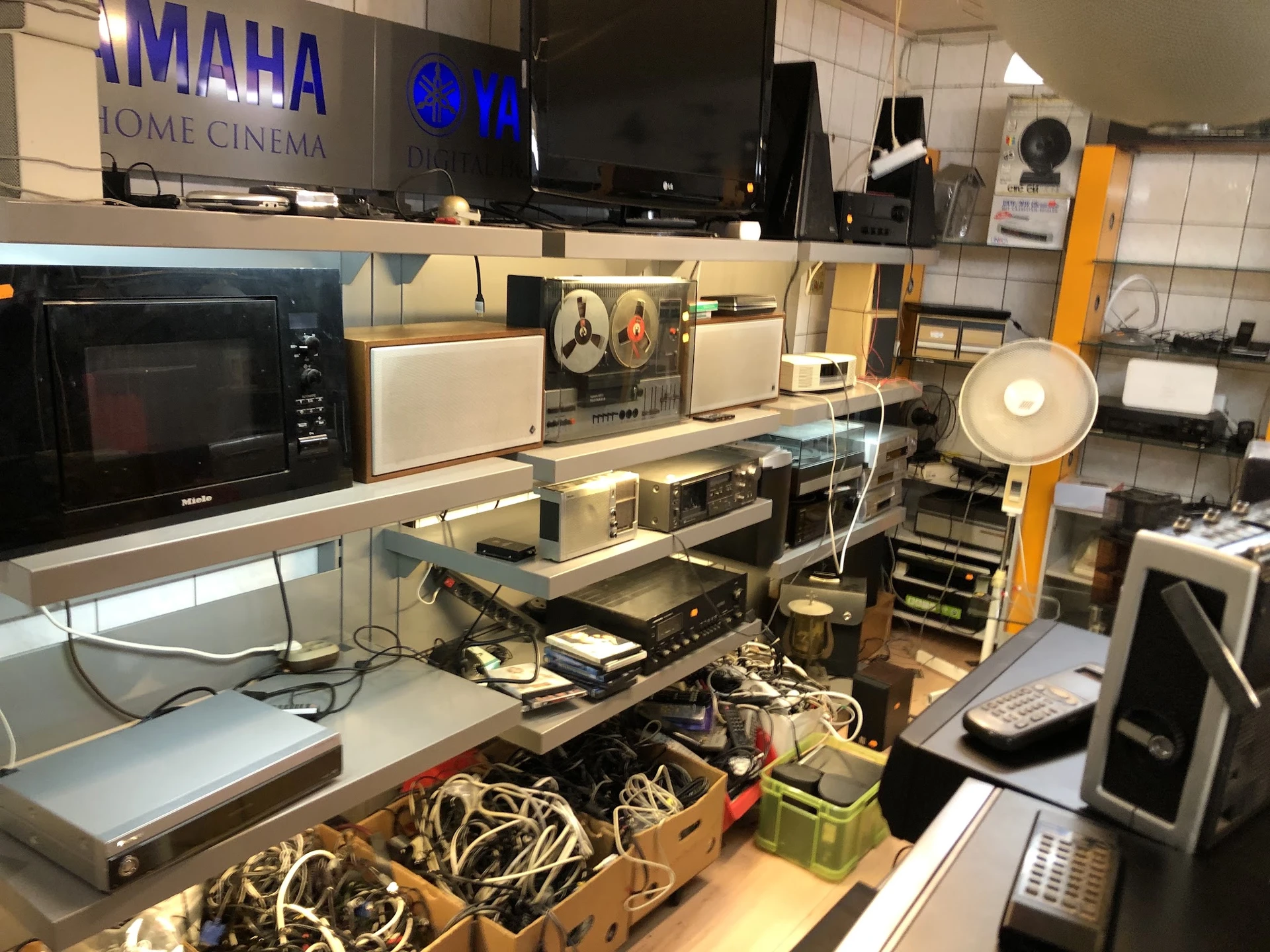 Uitgestalde elektronica en huishoudelijke apparaten op planken en tafels in de winkel