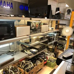 Uitgestalde elektronica en huishoudelijke apparaten op planken en tafels in de winkel