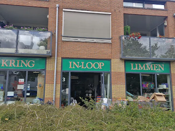 Gevel van kringloopwinkel met groene winkelruit en opschriften, voorkant mede zichtbaar vanuit straat