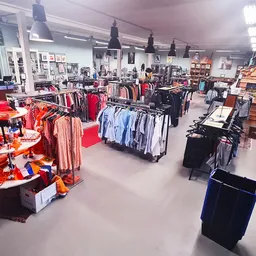 Ruim winkelbinnenland met kledingrekken, rode displays en zwarte hangende lampen