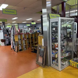 Winkelvloer met houten stellingen vol met kleding, schoenen en accessoires, fluorescerende gele borden en een glazen vitrinek