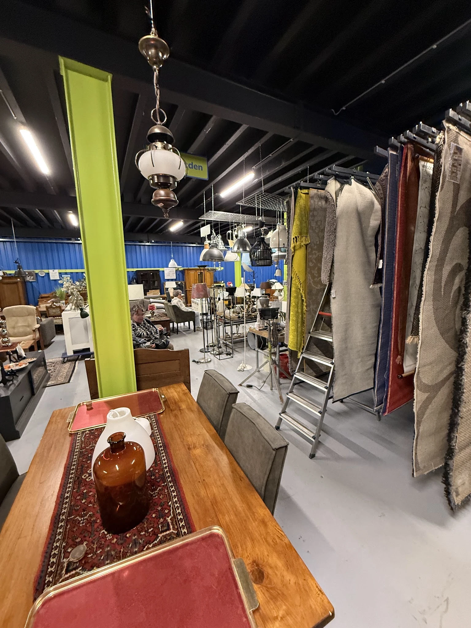Winkelvloer met kleding op rekken, eettafel met servies en lampen in kringloopwinkel