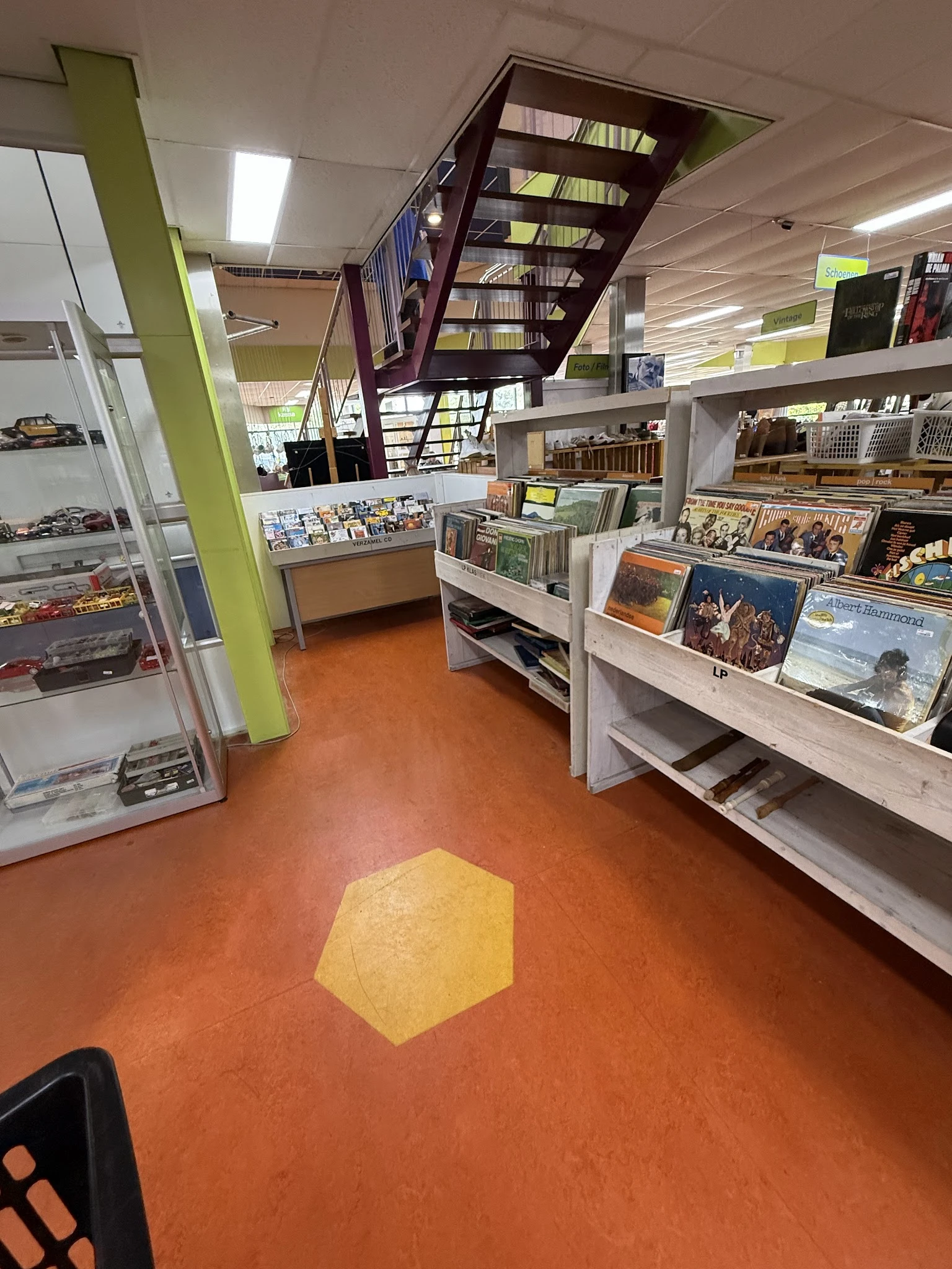 Winkelvloer met stellingen vol boeken, dvd's en andere tweedehands artikelen, oranje vloer met geel markeringsstrook