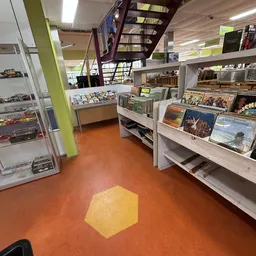 Winkelvloer met stellingen vol boeken, dvd's en andere tweedehands artikelen, oranje vloer met geel markeringsstrook
