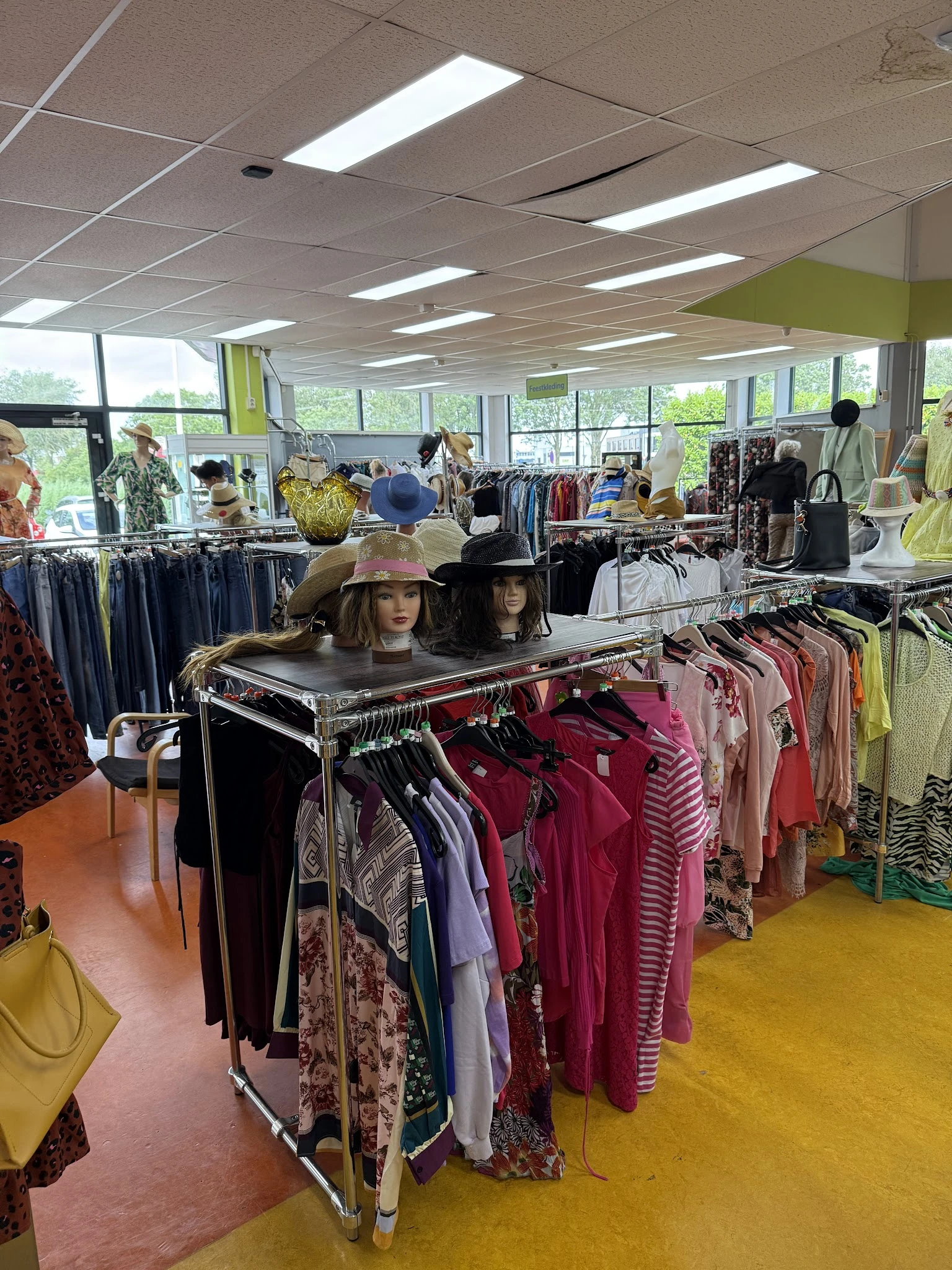 Winkelvloer met kledingrekken, mannequins en kleding in een kringloopwinkel met grote ramen
