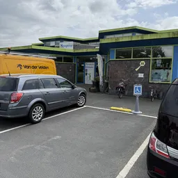 Voorkant van kringloopwinkel met groene en zwarte gevel, parkeerplaats met auto's en fietsen