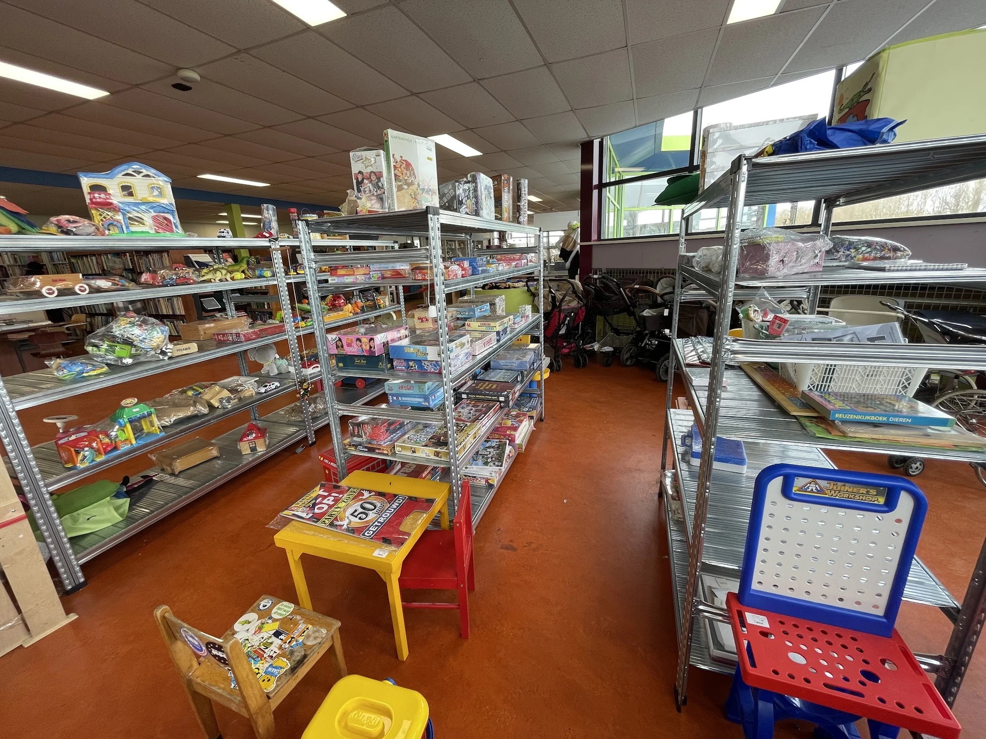 Winkelvloer van kringloopwinkel met metalen stellingen vol spullen, gele en rode speelgoedkisten op de grond
