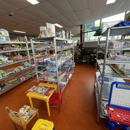 Winkelvloer van kringloopwinkel met metalen stellingen vol spullen, gele en rode speelgoedkisten op de grond