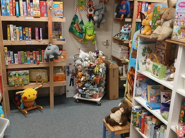Winkelinterieur met boekenkasten, speelgoed, boeken en verzamelaarsitems op stellingen en in een winkelwagen