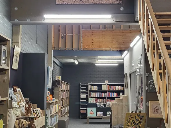Winkelinterieur met boekenkasten, stellingen met boeken en media, verlichte plafondpanelen en houten trap rechts