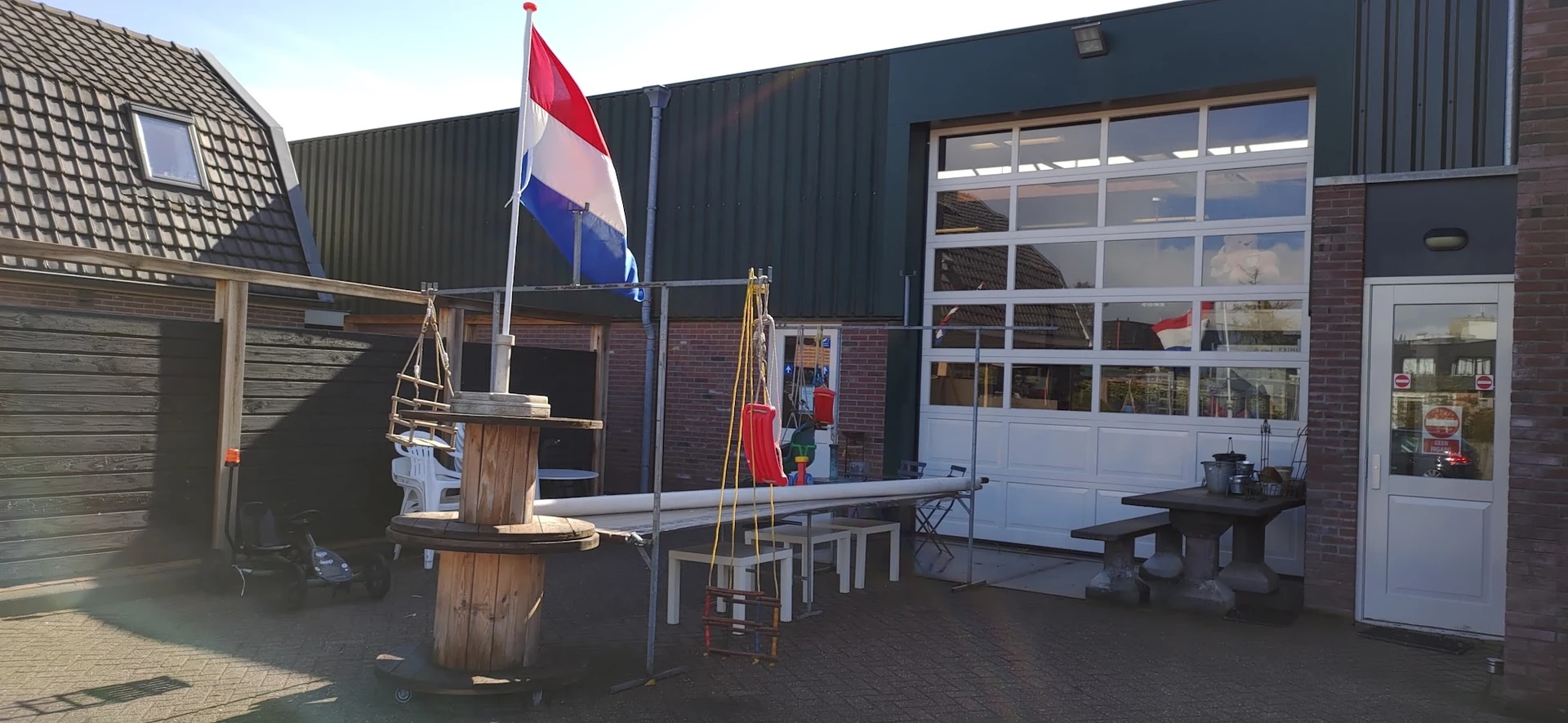 Voorkant kringloopwinkel met Nederlandse vlag, houten decoratie en terras met tafels en bankjes