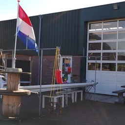 Voorkant kringloopwinkel met Nederlandse vlag, houten decoratie en terras met tafels en bankjes
