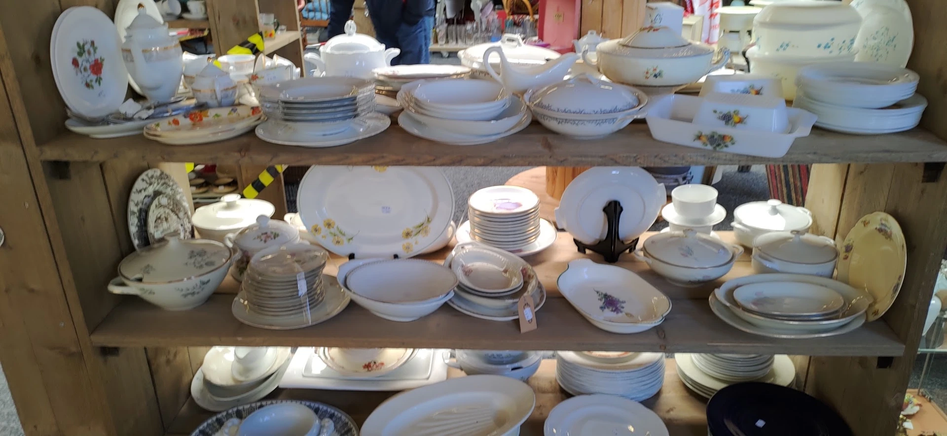 Uitgestalde serviesgoed op tafels: witte borden, kommen, schalen en tureens met bloemenpatronen