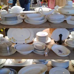 Uitgestalde serviesgoed op tafels: witte borden, kommen, schalen en tureens met bloemenpatronen