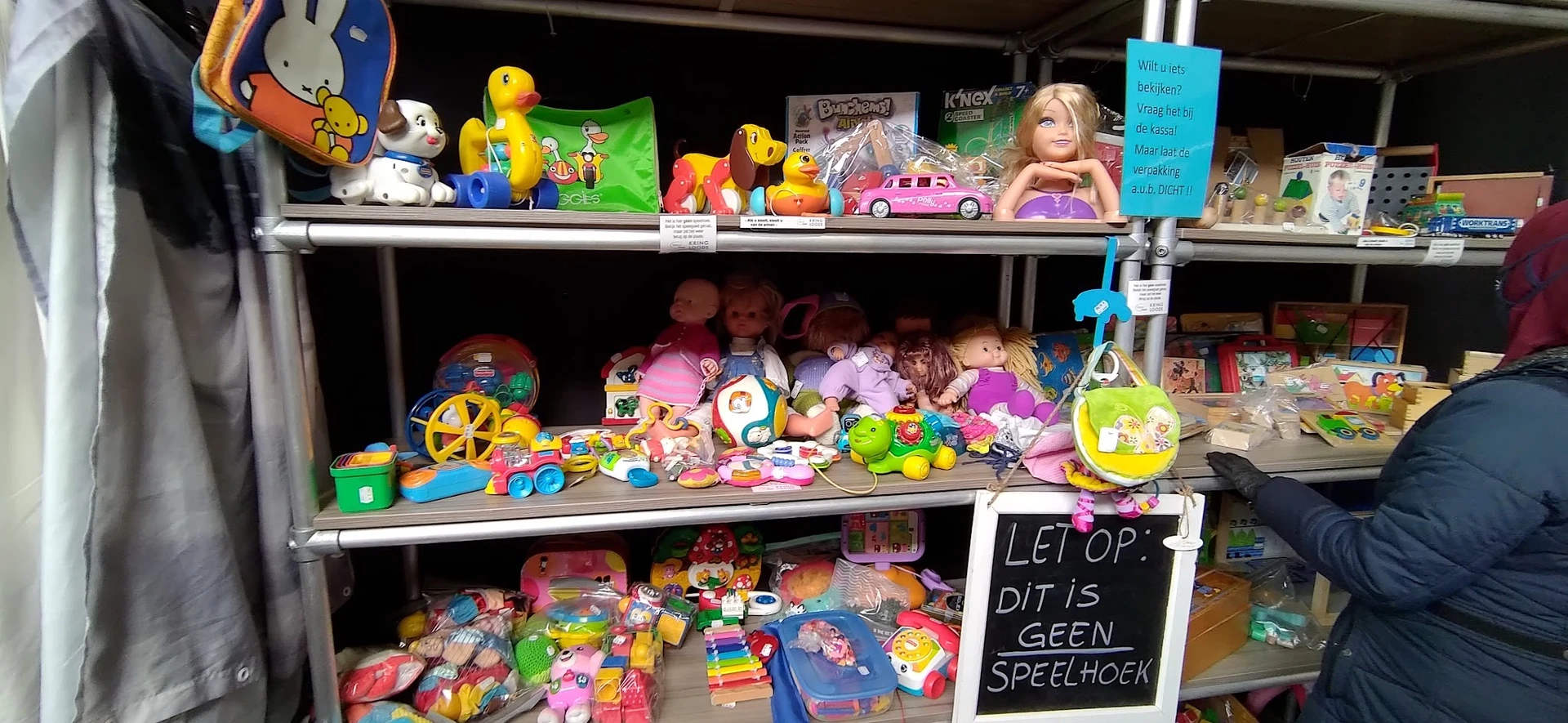 Stellingen met tweedehands speelgoed, waaronder poppen, auto's, poppenhuis en diverse plastic speeltjes