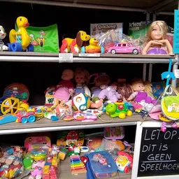 Stellingen met tweedehands speelgoed, waaronder poppen, auto's, poppenhuis en diverse plastic speeltjes