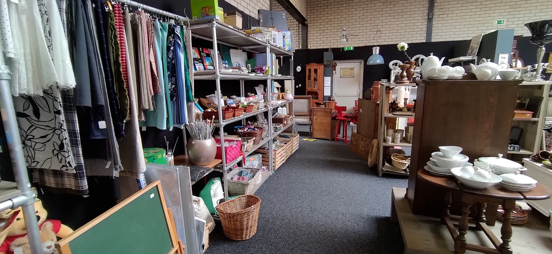 Winkelvloer met stellingen vol kleding, huishoudartikelen en diverse tweedehands spullen