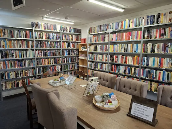 Boekenrekken langs de muren van een kringloopwinkel met een leestafels en zithoeken in het midden