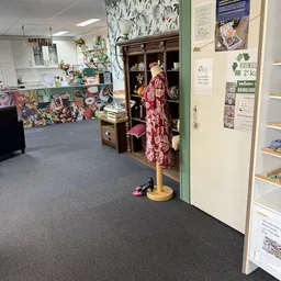 Winkelvloer met uitgestalde artikelen, mannequin in rode jurk, houten kast en diverse spullen in kringloopwinkel