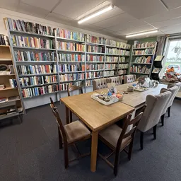 Leesruimte met houten tafel, grijze stoelen en boekenkasten langs de wanden in kringloopwinkel