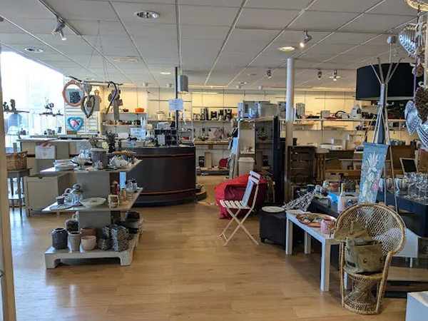 Winkelinterieur met houten vloer, diverse rekken, tafels met tweedehands spullen, verlichting van boven, rood kleedje
