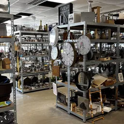 Stellingen met tweedehands huishoudspullen, klokken, decoratie en diverse artikelen in de kringloopwinkel