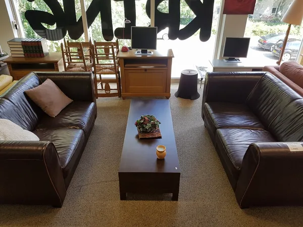 Woonkamer met twee bruine leren banken, salontafel en houten stoelen in kringloopwinkel