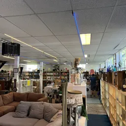 Binnenaanzicht van kringloopwinkel met bruine bank, boekenkasten, display-kasten en verschillende meubels en spullen uitgesta