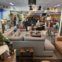 Ruim winkelbinnenland met grijs zitmeubel, houten salontafel, boeken, lampen en diverse meubelen en decoratie