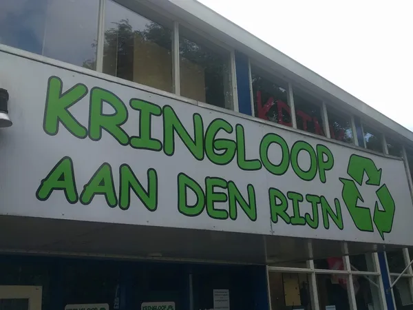 Gevel van kringloopwinkel met groene letters 'KRINGLOOP AAN DEN RIJN' en recyclesymbool