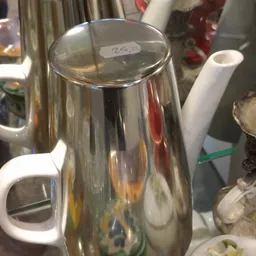 Close-up van een zilveren theepot met witte handvaten en een prijskaartje