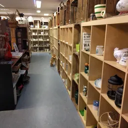Winkelinterieur met houten stellingen vol huishoudelijke items en decoratie, grijze vloer, poster aan wand