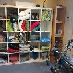 Witte open stellingkast met vakken vol opgevouwen kleding, kussens en huishoudtextiel in verschillende kleuren