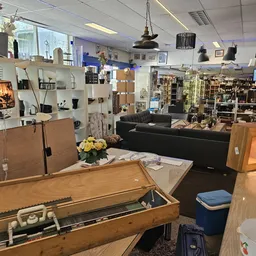 Ruim interieur van kringloopwinkel met stellingen vol spullen, zwarte bank, houten meubels en diverse artikelen