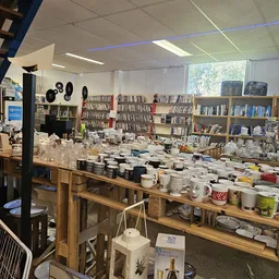 Werkruimte met lange houten tafel vol items, boekenkasten op achtergrond, ramen met daglicht