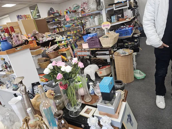 Rommelige winkelruimte met diverse tweedehandsspullen, decoraties en huishoudartikelen uitgestald op tafels en stellingen