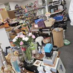 Rommelige winkelruimte met diverse tweedehandsspullen, decoraties en huishoudartikelen uitgestald op tafels en stellingen