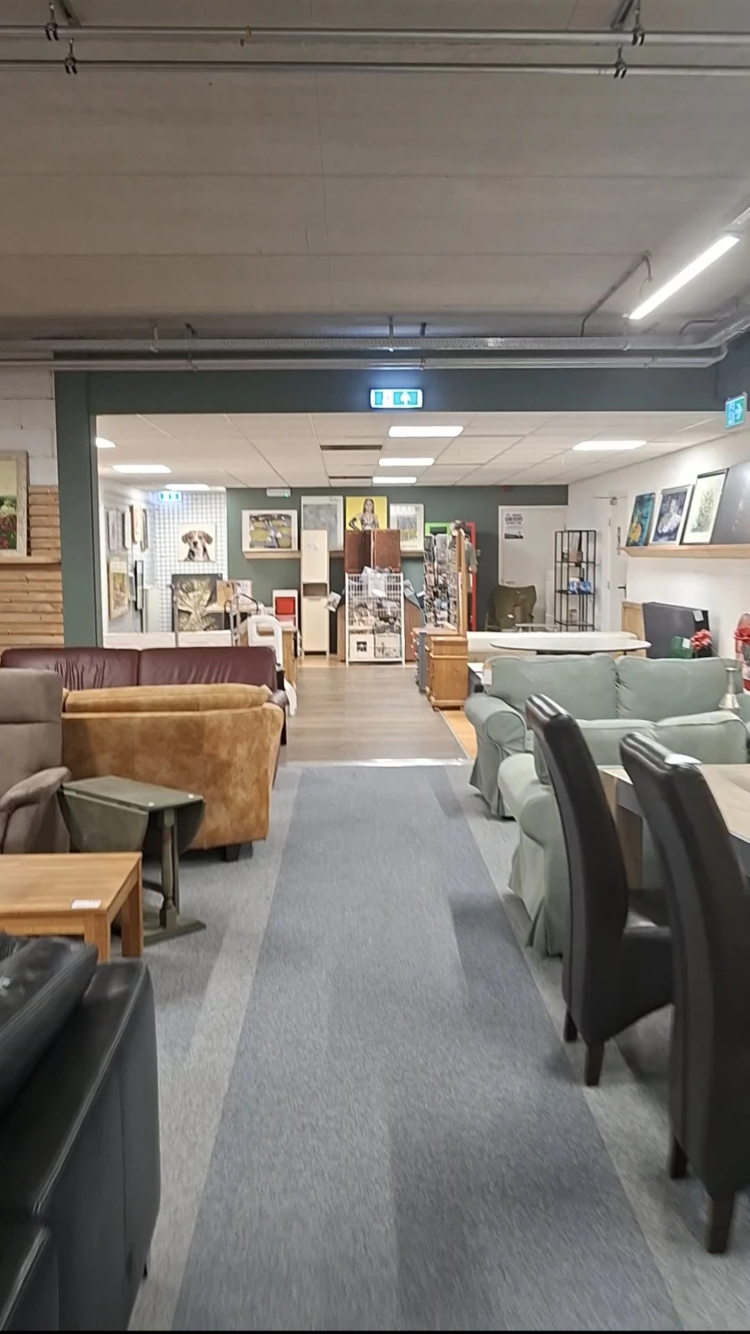 Winkelvloer met bruine en groene fauteuils, houten tafels, stellingen met decoraties en foto's aan de muren